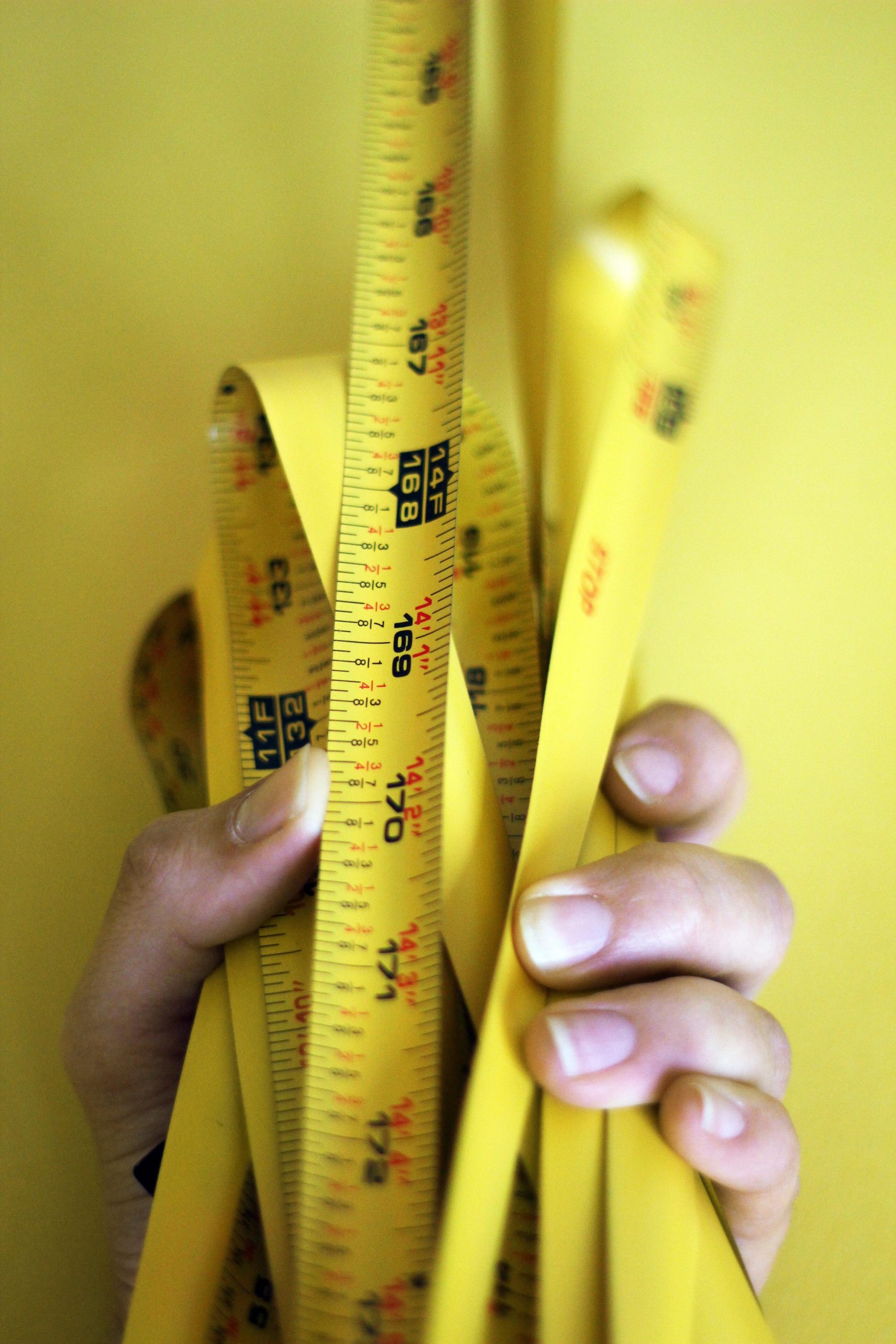 close of up folded yellow tape measure in man's hand Vivax Pros House Painters